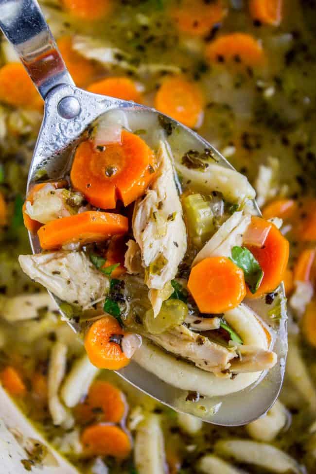 Chicken Noodle Soup with Homemade Noodles from The Food Charlatan. Is there anything more comforting than homemade Chicken Noodle Soup? Carrots, onions, celery...the smell is enough to bring you back. This recipe uses dark and white meat from a rotisserie chicken, and homemade noodles (or you can totally use store-bought). It's nostalgia in a bowl! #chicken #noodles #homemade #soup #comfortfood #healthy #easy #carrots #celery #rotisserie a metal spoon lifting homemade chicken noodle soup.