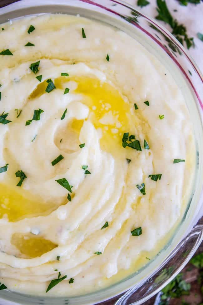 Creamy Mashed Potatoes from The Food Charlatan. My Aunt Shirley is famous for her mashed potatoes! They are SO creamy, fluffy, and have TONS of flavor. They are like soft pillowy clouds that melt in your mouth. I could describe them forever but you're just going to have to make them! A very unique recipe. #potatoes #mashed #creamy #butter #thanksgiving #comfortfood #creamcheese #easy #garlic #homemade #mashedpotatoes creamy mashed potatoes in a glass bowl with melted butter and parsley on top.