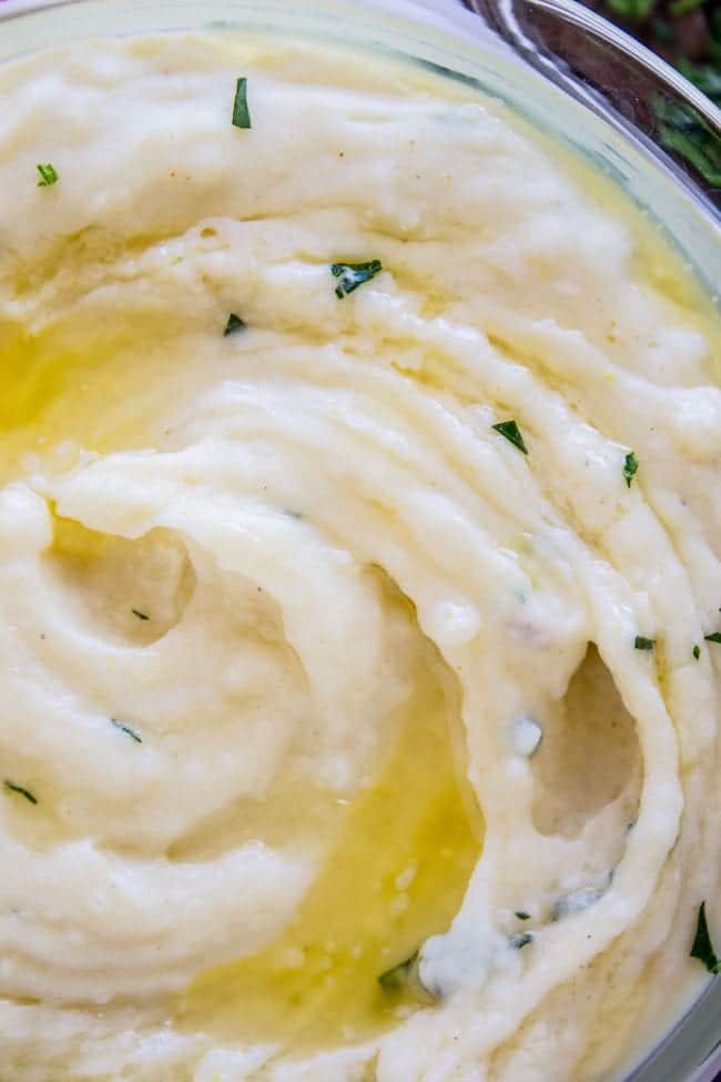 Creamy Mashed Potatoes from The Food Charlatan. My Aunt Shirley is famous for her mashed potatoes! They are SO creamy, fluffy, and have TONS of flavor. They are like soft pillowy clouds that melt in your mouth. I could describe them forever but you're just going to have to make them! A very unique recipe. #potatoes #mashed #creamy #butter #thanksgiving #comfortfood #creamcheese #easy #garlic #homemade #mashedpotatoes a glass bowl of creamy mashed potatoes with butter and parsley.