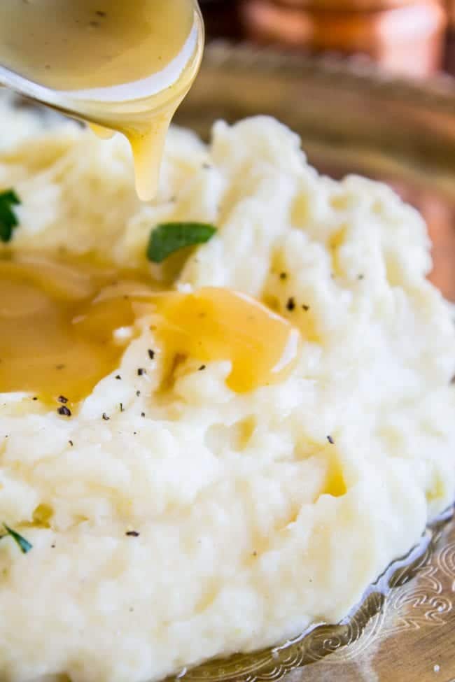 Creamy Mashed Potatoes from The Food Charlatan. My Aunt Shirley is famous for her mashed potatoes! They are SO creamy, fluffy, and have TONS of flavor. They are like soft pillowy clouds that melt in your mouth. I could describe them forever but you're just going to have to make them! A very unique recipe. #potatoes #mashed #creamy #butter #thanksgiving #comfortfood #creamcheese #easy #garlic #homemade #mashedpotatoes mashed potatoes with gravy being drizzled on top.