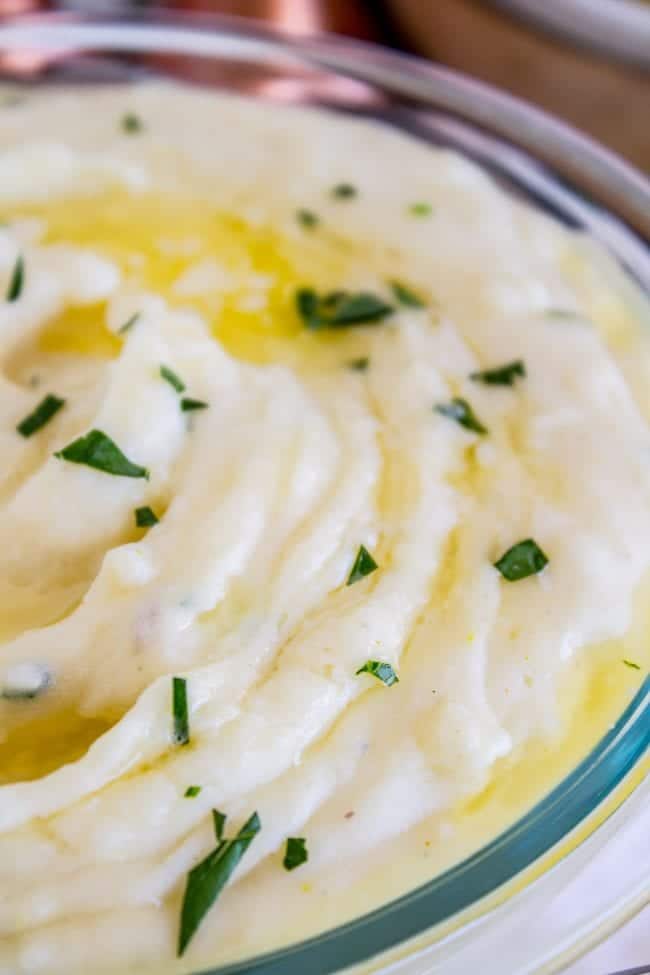 Creamy Mashed Potatoes from The Food Charlatan. My Aunt Shirley is famous for her mashed potatoes! They are SO creamy, fluffy, and have TONS of flavor. They are like soft pillowy clouds that melt in your mouth. I could describe them forever but you're just going to have to make them! A very unique recipe. #potatoes #mashed #creamy #butter #thanksgiving #comfortfood #creamcheese #easy #garlic #homemade #mashedpotatoes creamy mashed potatoes with butter and parsley on top in a glass bowl.