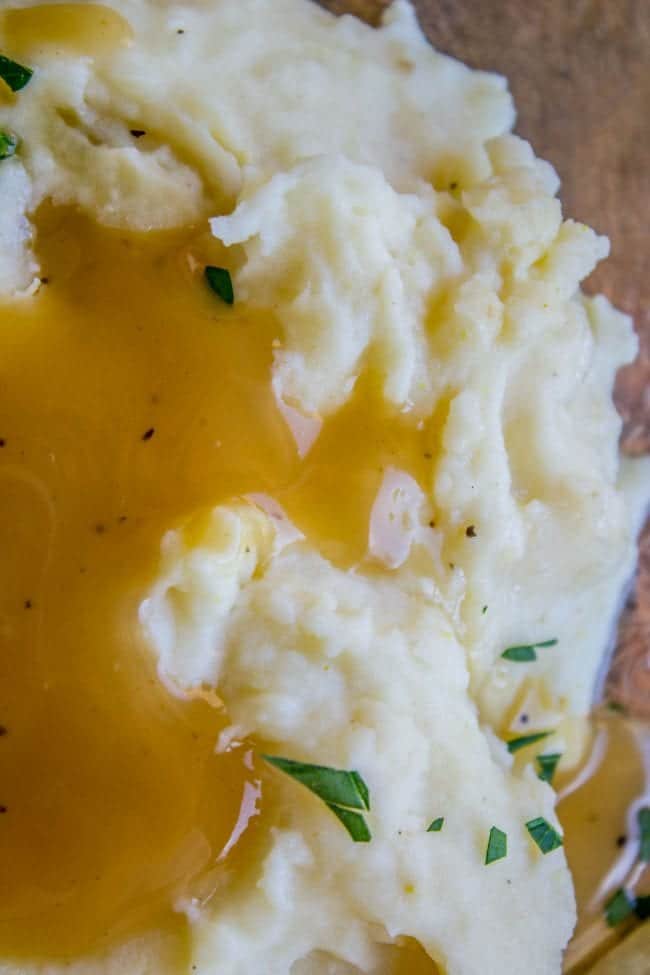 Creamy Mashed Potatoes from The Food Charlatan. My Aunt Shirley is famous for her mashed potatoes! They are SO creamy, fluffy, and have TONS of flavor. They are like soft pillowy clouds that melt in your mouth. I could describe them forever but you're just going to have to make them! A very unique recipe. #potatoes #mashed #creamy #butter #thanksgiving #comfortfood #creamcheese #easy #garlic #homemade #mashedpotatoes a pile of fluffy mashed potatoes with gravy on top.