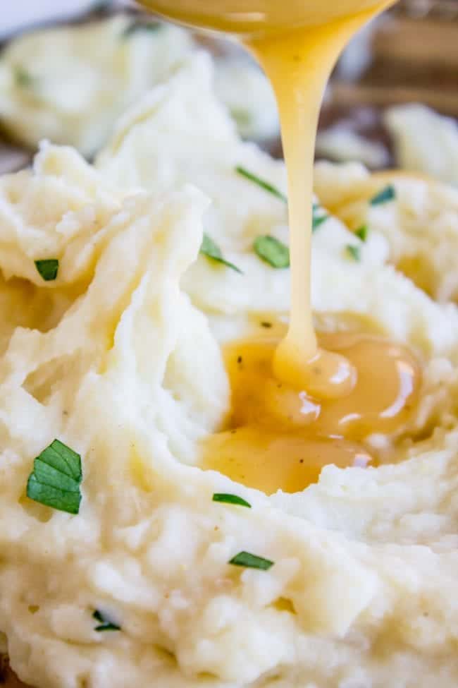 Creamy Mashed Potatoes from The Food Charlatan. My Aunt Shirley is famous for her mashed potatoes! They are SO creamy, fluffy, and have TONS of flavor. They are like soft pillowy clouds that melt in your mouth. I could describe them forever but you're just going to have to make them! A very unique recipe. #potatoes #mashed #creamy #butter #thanksgiving #comfortfood #creamcheese #easy #garlic #homemade #mashedpotatoes pouring gravy on creamy mashed potatoes.