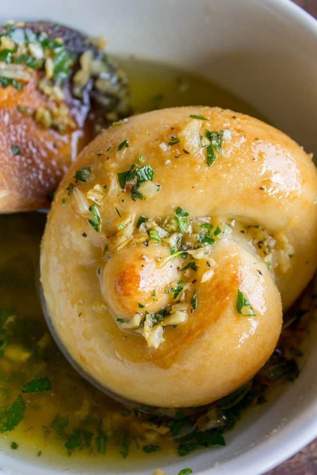 Garlic Knots Recipe from The Food Charlatan. These Garlic Knots are the perfect rolls for your Thanksgiving (or Easter) table! They are chewy and soft, and have TONS of garlicky, buttery flavor! You can't eat just one. (At least I can't. A batch of these rolls is basically a meal for me.) #garlic #bread #knots #rolls #homemade #fromscratch #dinner #holidays #thanksgiving #easter fresh homemade garlic knots being soaked in garlic parsley butter.