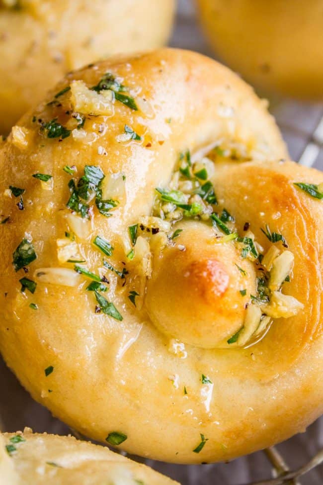 Garlic Knots from The Food Charlatan. These Garlic Knots are the perfect rolls for your Thanksgiving (or Easter) table! They are chewy and soft, and have TONS of garlicky, buttery flavor! You can't eat just one. (At least I can't. A batch of these rolls is basically a meal for me.) #garlic #bread #knots #rolls #homemade #fromscratch #dinner #holidays #thanksgiving #easter garlic knots with fresh parsley garlic butter.