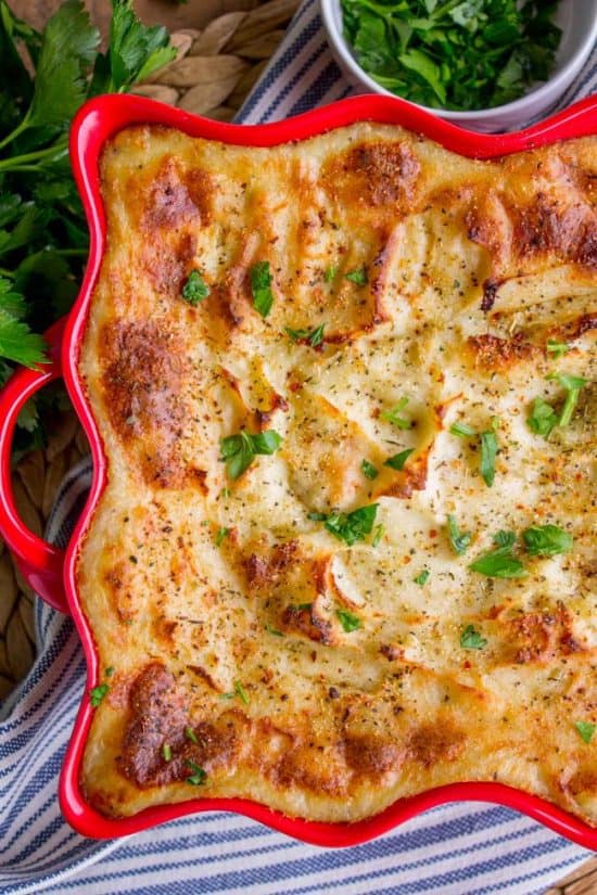 golden brown make ahead mashed potatoes in a red serving dish.