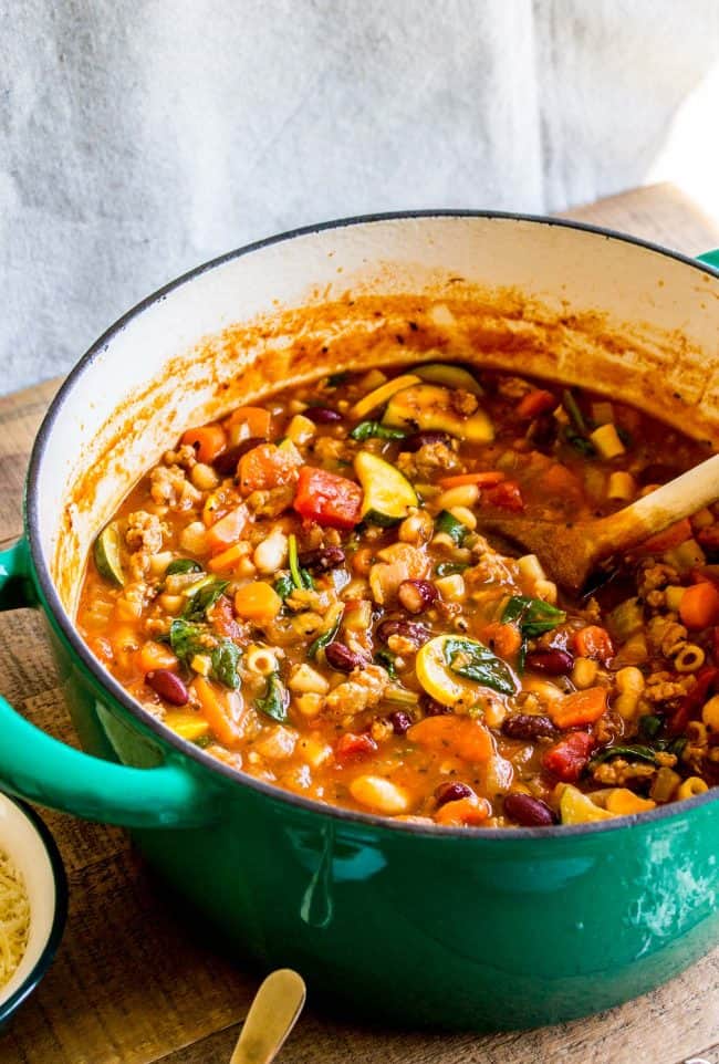 minestrone soup with sausage in a pot with a wooden spoon.