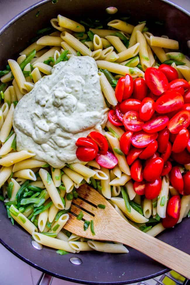 30 Minute Pesto Penne with Chicken and Cherry Tomatoes from The Food Charlatan. This 30 Minute Pesto Penne Chicken is your new favorite last minute dinner! It's done so quick, you can even used canned chicken if you are really crunched for time. Swap the frozen green beans and cherry tomatoes for whatever veggies you have on hand! #pesto #pasta #cherrytomatoes #easydinner #fast #greenbeans #chicken #penne #basil #greenonions #mayonnaise #skillet #dinner #easydinner #healthy #healthydinner bowl with penne, cherry tomatoes, creamy pesto sauce and herbs and a wooden spoon.