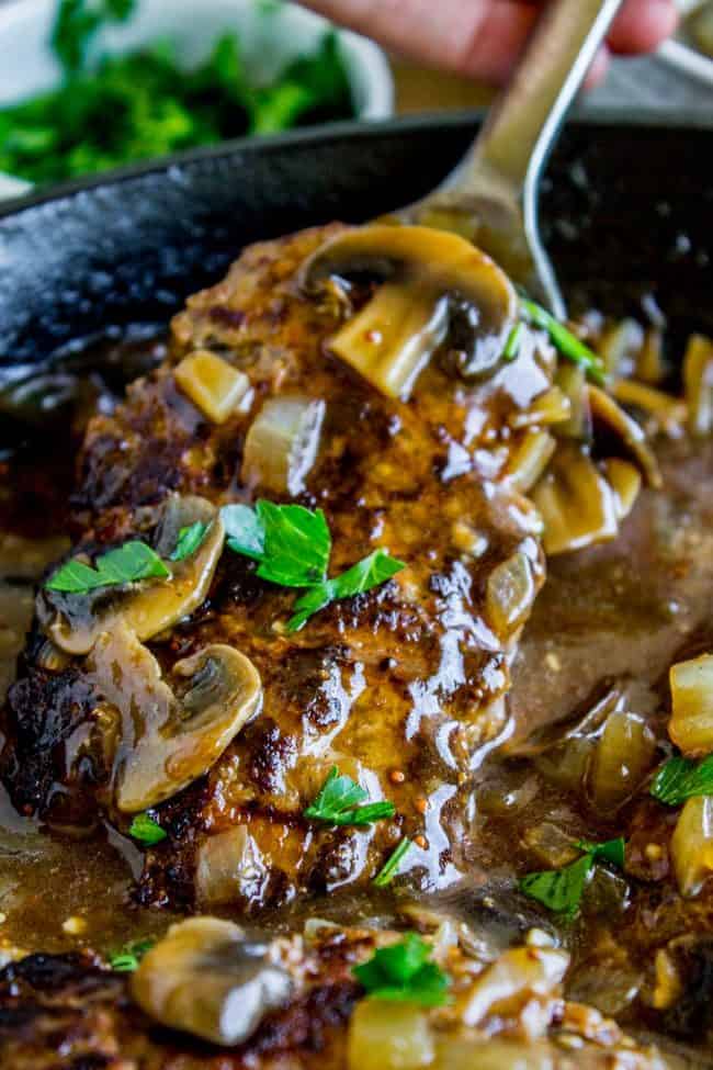 Salisbury Steak with Mushroom Gravy (30 Minute dinner) from The Food Charlatan. Salisbury Steak sounds so fancy but it's SO easy to make. They are basically mini meatloaves fried and served with mushroom gravy. It's the perfect comfort food and only takes 30 minutes to make. You have to serve this with Creamy Mashed Potatoes to get the full effect! #ComfortFood #Easy #30minutes #dinner #oneskillet #beef #groundbeef #mashedpotatoes #gravy #mushrooms #sauce #hamburger #fromscratch salisbury steak with mushroom gravy and fresh parsley in a cast iron skillet.