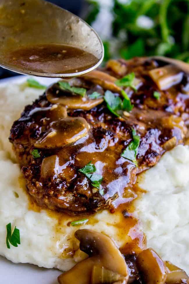 Salisbury Steak with Mushroom Gravy (30 Minute dinner) from The Food Charlatan. Salisbury Steak sounds so fancy but it's SO easy to make. They are basically mini meatloaves fried and served with mushroom gravy. It's the perfect comfort food and only takes 30 minutes to make. You have to serve this with Creamy Mashed Potatoes to get the full effect! #ComfortFood #Easy #30minutes #dinner #oneskillet #beef #groundbeef #mashedpotatoes #gravy #mushrooms #sauce #hamburger #fromscratch salisbury steak with mushroom gravy on top of creamy mashed potatoes.