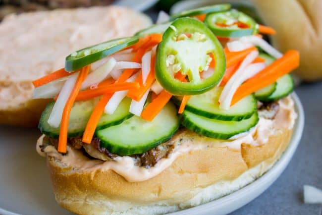 Banh Mi Sandwich from The Food Charlatan. These traditional Vietnamese Banh Mi Sandwiches will blow your mind! A mini soft baguette, smeared with sriracha mayo, topped with thinly sliced marinated pork, pickled veggies, and tons of cilantro. It's heaven! #vietnam #banhmi #sandwich #vietnamese #cilantro #daikon #pickled #carrots #baguette #recipe #pork #howtomake #pickledvegetables #sauce #sriracha #mayonnaise pork banh mi with the top bun open.