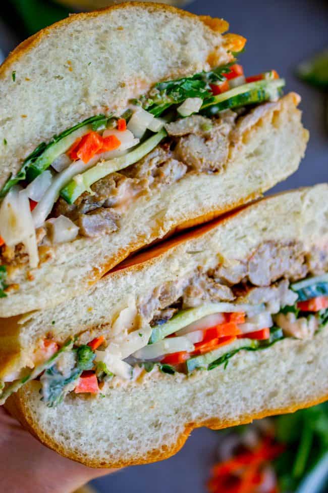 Banh Mi Sandwich from The Food Charlatan. These traditional Vietnamese Banh Mi Sandwiches will blow your mind! A mini soft baguette, smeared with sriracha mayo, topped with thinly sliced marinated pork, pickled veggies, and tons of cilantro. It's heaven! #vietnam #banhmi #sandwich #vietnamese #cilantro #daikon #pickled #carrots #baguette #recipe #pork #howtomake #pickledvegetables #sauce #sriracha #mayonnaise banh mi sandwich cut in half.
