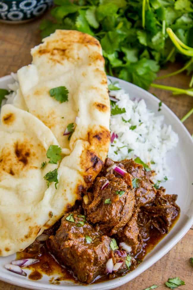 Slow Cooker Beef Curry from The Food Charlatan. This slow cooker beef curry could not be easier! Thick chunks of slow-cooked, tender beef, in a rich and thick curry sauce that is just waiting to be scooped up with some naan. #curry #beef #beefcurry #indian #indianfood #yellow #rice #naan #cilantro #tender #crockpot #slowcooker beef curry with cilantro, naan, and rice.