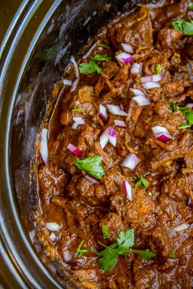 Slow Cooker Beef Curry from The Food Charlatan. This slow cooker beef curry could not be easier! Thick chunks of slow-cooked, tender beef, in a rich and thick curry sauce that is just waiting to be scooped up with some naan. #curry #beef #beefcurry #indian #indianfood #yellow #rice #naan #cilantro #tender #crockpot #slowcooker beef curry in a slow cooker with red onion and cilantro.