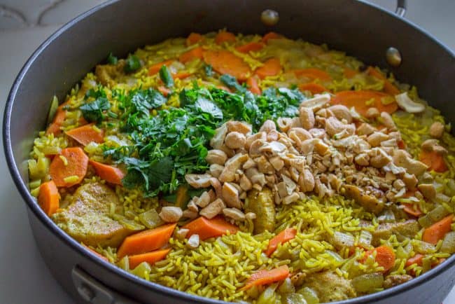 Chicken Biryani (30 Minute Indian Chicken & Rice) from The Food Charlatan. This stove top Chicken Biryani is a delicious 30 minute dinner! You could also call it Indian Chicken and Rice. It's so easy to make and is a healthy weeknight dinner that everyone will love! #chicken #chickendinner #easy #recipe #indian #indianfood #30minutes #dinner #healthy #carrots #onion #cilantro #cashew #stovetop #oneskillet #onepot #rice #basmati #spices #curry #vegetable #skillet adding cilantro and cashews to chicken biryani.