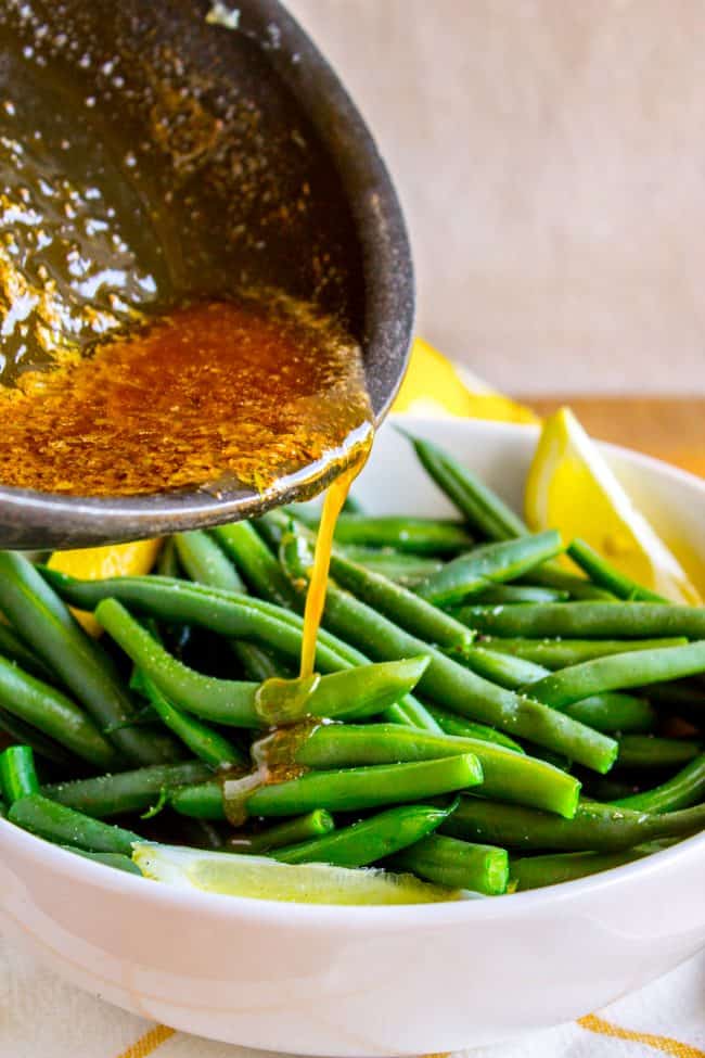 Lemon Dijon Green Beans Almondine from The Food Charlatan. Lemon Dijon Green Beans Almondine is super easy and has tons of flavor! How can you go wrong with butter (and maybe browning it a little?) and lemon and Dijon? You can even make this ahead of time if you plan to serve it for Thanksgiving dinner. #greenbean #almondine #almond #beans #lemon #dijon #mustard #garlic #brownedbutter #butter #sidedish #Thanksgiving #sauteed #fresh #healthy #easy #recipes #withalmonds pouring browned butter over blanched green beans.