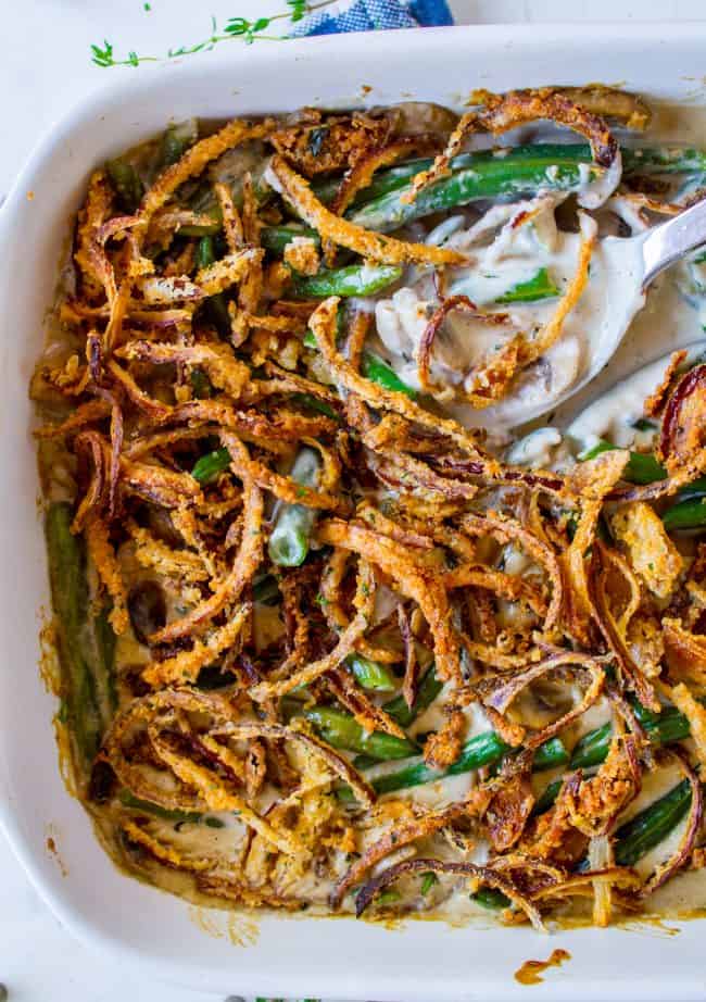 Homemade Green Bean Casserole Recipe from The Food Charlatan. Not your mama's Green Bean Casserole recipe! Let's kick that can of soup out to the curb because the homemade version is LEGIT you guys. Big, bright green beans in a creamy mushroom sauce, topped with crispy fried onions. Thanksgiving doesn't get any better than this! #greenbeans #casserole #frenchs #fromscratch #homemade #thanksgiving #sidedish #easy #fresh #recipe #classic #best #withcheese #foracrowd #makeahead #simple #classic #creamy green bean casserole with homemade crispy fried onions and a serving spoon.