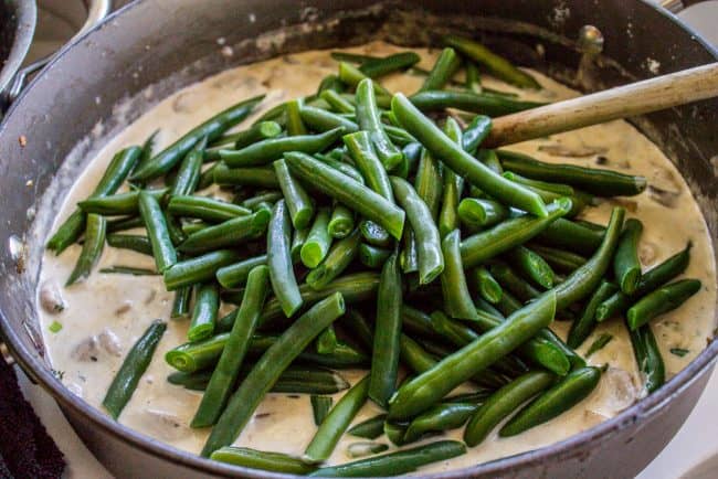 Homemade Green Bean Casserole Recipe from The Food Charlatan. Not your mama's Green Bean Casserole recipe! Let's kick that can of soup out to the curb because the homemade version is LEGIT you guys. Big, bright green beans in a creamy mushroom sauce, topped with crispy fried onions. Thanksgiving doesn't get any better than this! #greenbeans #casserole #frenchs #fromscratch #homemade #thanksgiving #sidedish #easy #fresh #recipe #classic #best #withcheese #foracrowd #makeahead #simple #classic #creamy adding blanched green beans to creamy mushroom sauce.