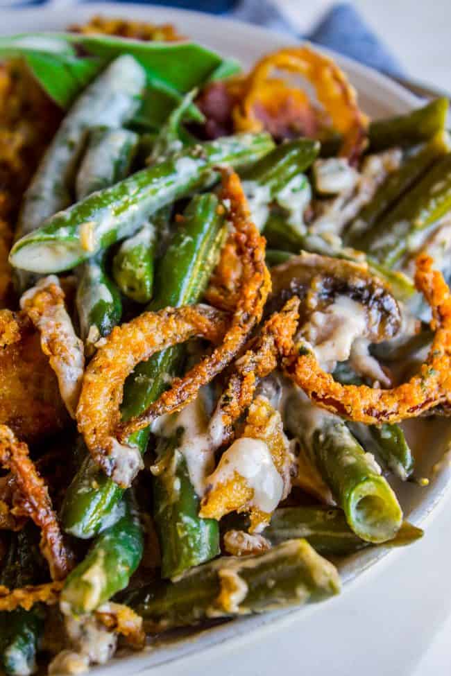 Homemade Green Bean Casserole Recipe from The Food Charlatan. Not your mama's Green Bean Casserole recipe! Let's kick that can of soup out to the curb because the homemade version is LEGIT you guys. Big, bright green beans in a creamy mushroom sauce, topped with crispy fried onions. Thanksgiving doesn't get any better than this! #greenbeans #casserole #frenchs #fromscratch #homemade #thanksgiving #sidedish #easy #fresh #recipe #classic #best #withcheese #foracrowd #makeahead #simple #classic #creamy green bean casserole from scratch with crispy fried onions on top.