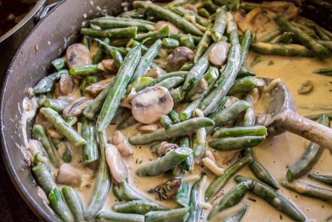 Homemade Green Bean Casserole Recipe from The Food Charlatan. Not your mama's Green Bean Casserole recipe! Let's kick that can of soup out to the curb because the homemade version is LEGIT you guys. Big, bright green beans in a creamy mushroom sauce, topped with crispy fried onions. Thanksgiving doesn't get any better than this! #greenbeans #casserole #frenchs #fromscratch #homemade #thanksgiving #sidedish #easy #fresh #recipe #classic #best #withcheese #foracrowd #makeahead #simple #classic #creamy a mixture of green beans, parmesan cheese, and creamy mushroom sauce in a skillet.