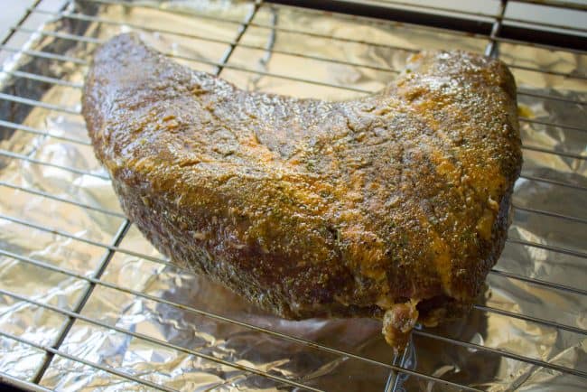 raw tri tip roast with seasoning on a rack over tin foil.