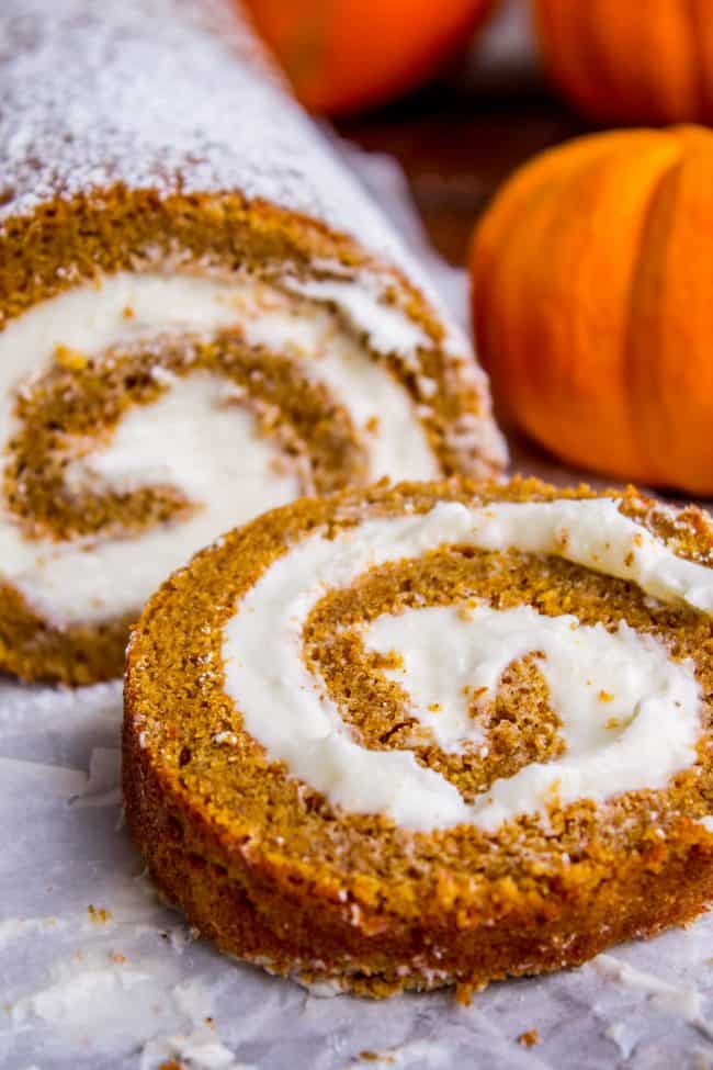 Pumpkin Roll Recipe with Lots of Cream Cheese Frosting from The Food Charlatan. This easy Pumpkin Roll recipe is so impressive and delicious! It's a classic Thanksgiving dessert that you definitely need to make this year. I used LOTS of cream cheese frosting so that it's super moist! #pumpkin #roll #creamcheese #icing #frosting #thanksgiving #christmas #fall #fallbaking #recipe #withcreamcheesefilling #easy #withnutmeg #Libbys #best #homemade #classic #moist #gift #perfect #howtomake #cinnamon pumpkin roll with cream cheese frosting, with one slice cut.