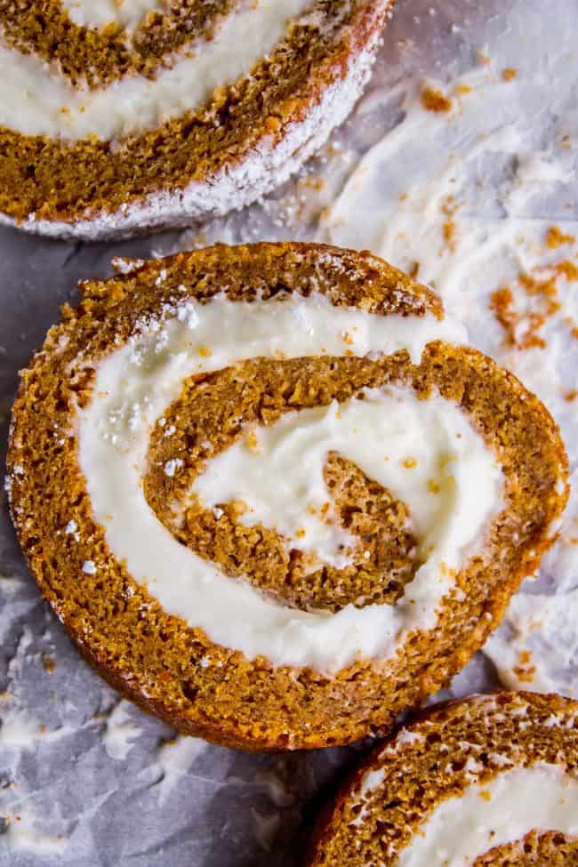 Pumpkin Roll Recipe with Lots of Cream Cheese Frosting from The Food Charlatan. This easy Pumpkin Roll recipe is so impressive and delicious! It's a classic Thanksgiving dessert that you definitely need to make this year. I used LOTS of cream cheese frosting so that it's super moist! #pumpkin #roll #creamcheese #icing #frosting #thanksgiving #christmas #fall #fallbaking #recipe #withcreamcheesefilling #easy #withnutmeg #Libbys #best #homemade #classic #moist #gift #perfect #howtomake #cinnamon pumpkin roll dusted with powdered sugar, cut into slices.