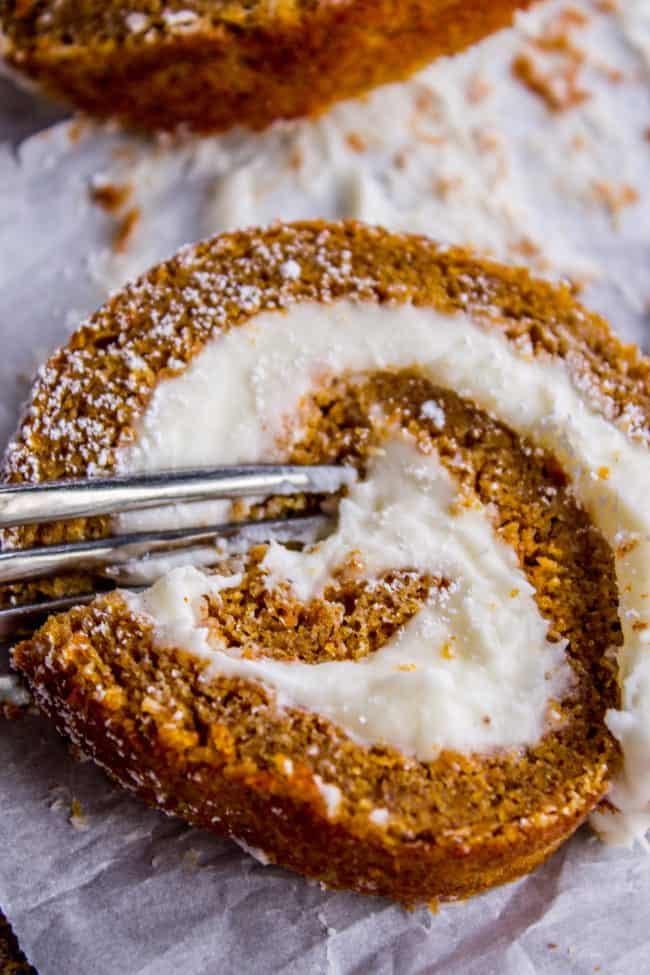 Pumpkin Roll Recipe with Lots of Cream Cheese Frosting from The Food Charlatan. This easy Pumpkin Roll recipe is so impressive and delicious! It's a classic Thanksgiving dessert that you definitely need to make this year. I used LOTS of cream cheese frosting so that it's super moist! #pumpkin #roll #creamcheese #icing #frosting #thanksgiving #christmas #fall #fallbaking #recipe #withcreamcheesefilling #easy #withnutmeg #Libbys #best #homemade #classic #moist #gift #perfect #howtomake #cinnamon a slice of pumpkin roll with a fork in it.