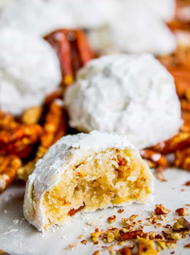 Mexican wedding cookies, one with a bite taken out, and pecans in the background.