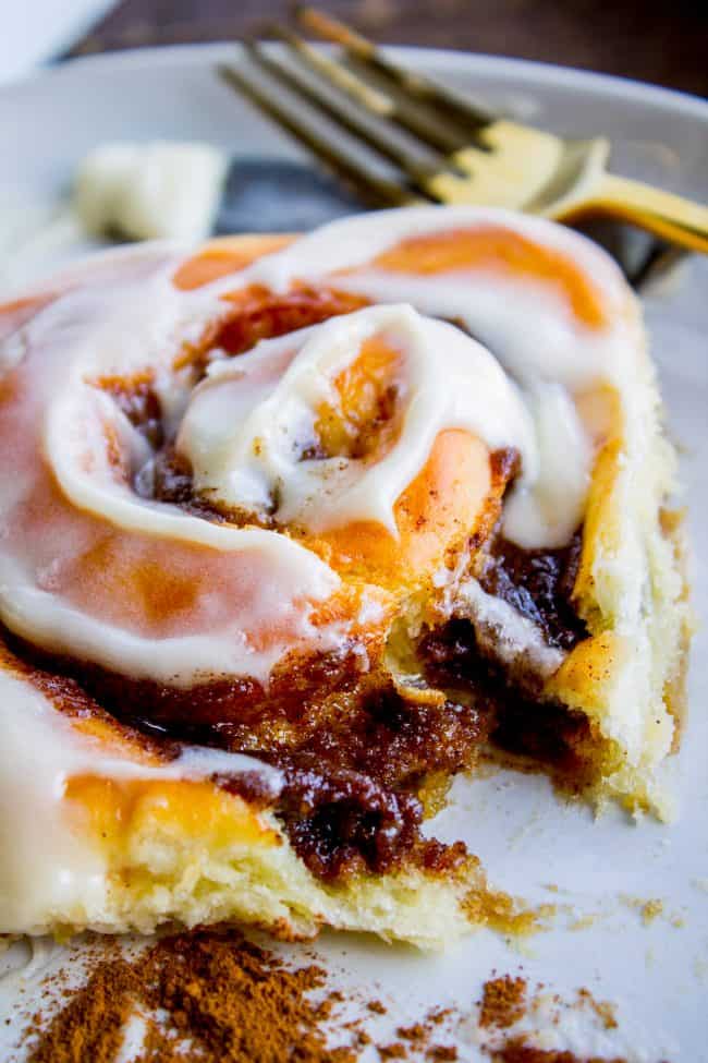 The FLUFFIEST Homemade Cinnamon Rolls of Your Life (Can Make Overnight) from The Food Charlatan. If you haven't made cinnamon rolls with a simple sweet dough (brioche style) instead of regular bread dough, you are totally missing out. These are the FLUFFIEST homemade cinnamon rolls of your life! They are very easy, and you can make them overnight! #cinnamon #cinnamonrolls #creamcheese #frosting #homemade #fluffy #gooey #easy #overnight #cinnabon #recipe #best #fromscratch #icing #makeahead fluffy iced cinnamon roll on a plate with a fork in the background.