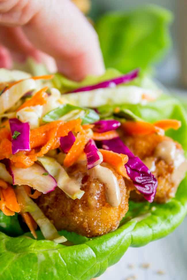 Thai Lettuce Wraps with Crispy Fish and Peanut Sauce from The Food Charlatan. These are a fabulous way to start off your January! Supple butter lettuce wrapped around crispy baked fish, topped with a gingery homemade Asian slaw. Drizzle with sweet and spicy Thai Peanut Sauce and you have an easy and healthy Asian-inspired weeknight dinner! #healthy #fish #crispy #cabbage #slaw #asian #Thai #peanutsauce #easy #sauce #lowcarb #lunch #simple #butterlettuce #greenonion #carrot #purplecabbage close up shot of a Thai lettuce wrap.