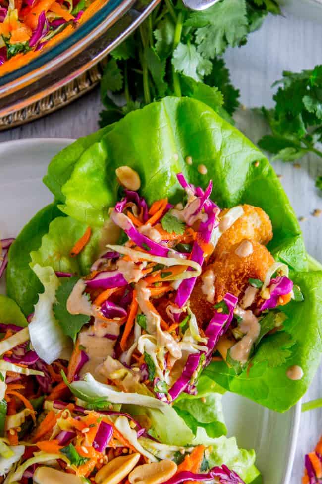 Thai Lettuce Wraps with Crispy Fish and Peanut Sauce from The Food Charlatan. These are a fabulous way to start off your January! Supple butter lettuce wrapped around crispy baked fish, topped with a gingery homemade Asian slaw. Drizzle with sweet and spicy Thai Peanut Sauce and you have an easy and healthy Asian-inspired weeknight dinner! #healthy #fish #crispy #cabbage #slaw #asian #Thai #peanutsauce #easy #sauce #lowcarb #lunch #simple #butterlettuce #greenonion #carrot #purplecabbage peanut sauce drizzled on top of a fish taco.
