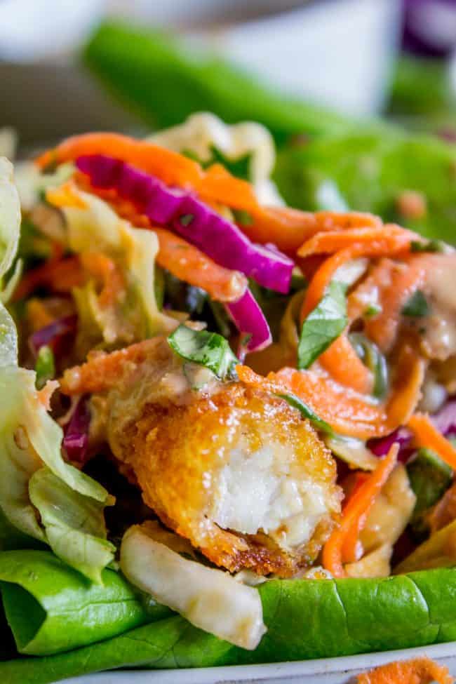 Thai Lettuce Wraps with Crispy Fish and Peanut Sauce from The Food Charlatan. These are a fabulous way to start off your January! Supple butter lettuce wrapped around crispy baked fish, topped with a gingery homemade Asian slaw. Drizzle with sweet and spicy Thai Peanut Sauce and you have an easy and healthy Asian-inspired weeknight dinner! #healthy #fish #crispy #cabbage #slaw #asian #Thai #peanutsauce #easy #sauce #lowcarb #lunch #simple #butterlettuce #greenonion #carrot #purplecabbage close up shot of a Thai lettuce wrap.
