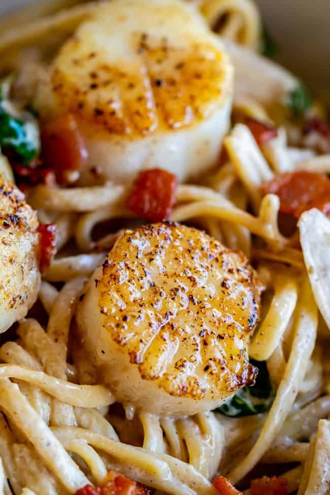 Pan Seared Scallops in Creamy Champagne Sauce from The Food Charlatan. If you have never paired tender, buttery, pan seared scallops with a creamy wine sauce, you are missing out! Toss with some linguine and crispy crumbled bacon, and you have a very special dinner for two. #valentinesday #valentine #dinnerfortwo #romantic #scallops #recipe #easy #pansear #seafood #seared #healthy #pasta #Howtocook #dinner #easy #fried #best #sauteed #creamy #spinach #meal #whattoserve #whitewine #champagne seared scallops in a creamy wine sauce with bacon and spinach over linguine.
