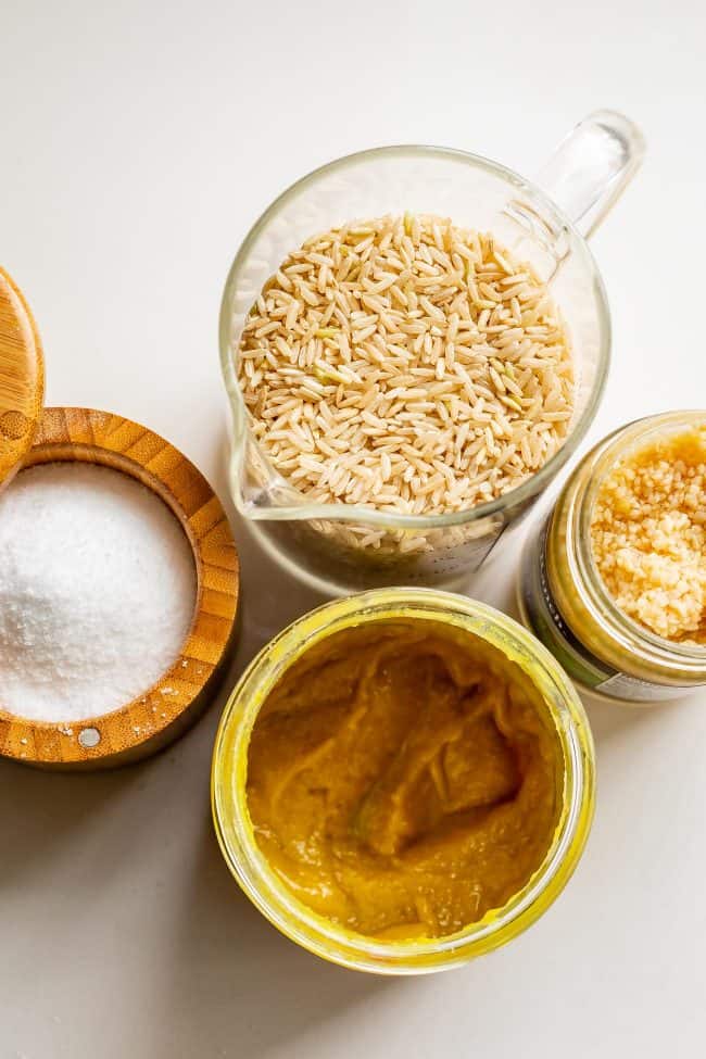 brown rice in a measuring cup with garlic, salt, and Better than Bouillon chicken base.