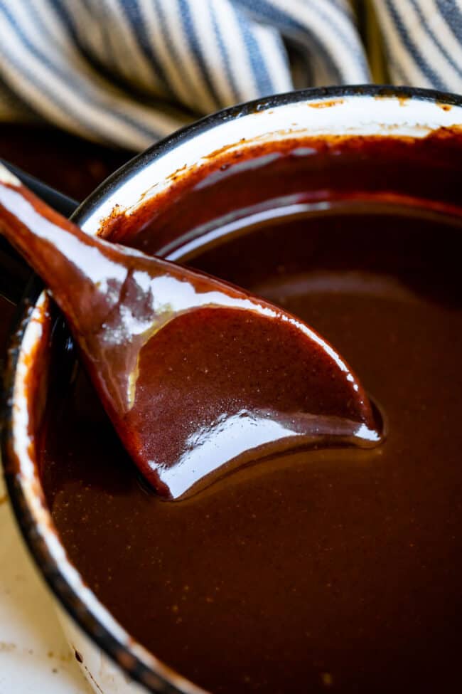 Homemade Chocolate Sauce (The Only Hot Fudge Sauce You'll Ever Need) from The Food Charlatan. Once you go homemade, there's NO going back! This recipe is super easy, uses pantry ingredients, and takes 15 minutes. It's 10x better than store bought hot fudge sauce. It's creamy, smooth, and so chocolatey. #hotfudge #fudge #hot #icecream #Toppings #sauce #homemade #recipe #chocolate #Chocolatesauce #easy #desserts #sundae #uses #oldfashioned #withevaporatedmilk #best #topping #nocornsyrup chocolate sauce in a pot with a spoon.