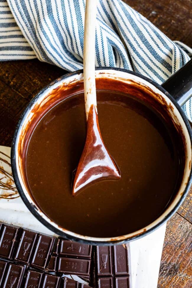 Homemade Chocolate Sauce (The Only Hot Fudge Sauce You'll Ever Need) from The Food Charlatan. Once you go homemade, there's NO going back! This recipe is super easy, uses pantry ingredients, and takes 15 minutes. It's 10x better than store bought hot fudge sauce. It's creamy, smooth, and so chocolatey. #hotfudge #fudge #hot #icecream #Toppings #sauce #homemade #recipe #chocolate #Chocolatesauce #easy #desserts #sundae #uses #oldfashioned #withevaporatedmilk #best #topping #nocornsyrup hot fudge sauce with a wooden spoon in a pot.