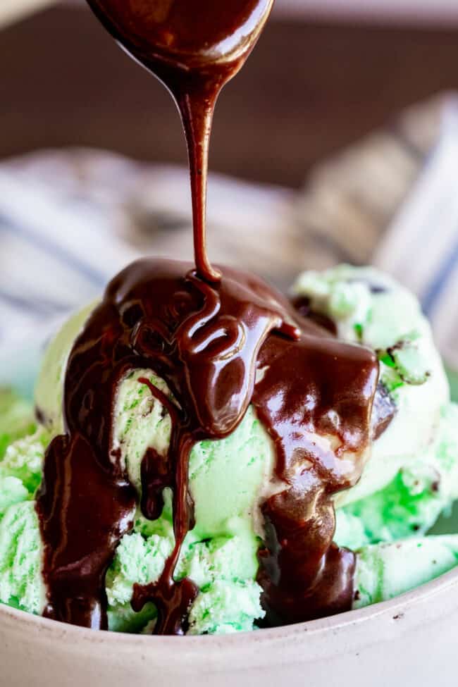 Homemade Chocolate Sauce (The Only Hot Fudge Sauce You'll Ever Need) from The Food Charlatan. Once you go homemade, there's NO going back! This recipe is super easy, uses pantry ingredients, and takes 15 minutes. It's 10x better than store bought hot fudge sauce. It's creamy, smooth, and so chocolatey. #hotfudge #fudge #hot #icecream #Toppings #sauce #homemade #recipe #chocolate #Chocolatesauce #easy #desserts #sundae #uses #oldfashioned #withevaporatedmilk #best #topping #nocornsyrup drizzling hot fudge sauce over mint chocolate chip ice cream.