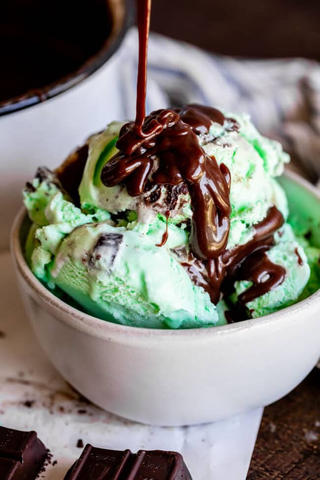 Homemade Chocolate Sauce (The Only Hot Fudge Sauce You'll Ever Need) from The Food Charlatan. Once you go homemade, there's NO going back! This recipe is super easy, uses pantry ingredients, and takes 15 minutes. It's 10x better than store bought hot fudge sauce. It's creamy, smooth, and so chocolatey. #hotfudge #fudge #hot #icecream #Toppings #sauce #homemade #recipe #chocolate #Chocolatesauce #easy #desserts #sundae #uses #oldfashioned #withevaporatedmilk #best #topping #nocornsyrup drizzling chocolate sauce on mint chocolate chip ice cream in a white bowl.