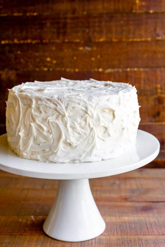 The Best Homemade White Cake Recipe of Your Life from The Food Charlatan. HALLELUJAH! Finally a moist white cake from scratch that doesn't taste like cardboard. I promise, this will be the best homemade white cake recipe of your life! It's soft and fluffy, while still being super moist. The balance of fluffy and moist is exactly perfect for how cake ought to be! It's fluffy yet full of buttery rich flavor. #white #cake #homemade #recipe #moist #fromscratch #easy #frosting #best #simple #perfect white cake with vanilla frosting on a cake stand.