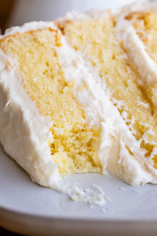 The Best Homemade White Cake Recipe of Your Life from The Food Charlatan. HALLELUJAH! Finally a moist white cake from scratch that doesn't taste like cardboard. I promise, this will be the best homemade white cake recipe of your life! It's soft and fluffy, while still being super moist. The balance of fluffy and moist is exactly perfect for how cake ought to be! It's fluffy yet full of buttery rich flavor. #white #cake #homemade #recipe #moist #fromscratch #easy #frosting #best #simple #perfect slice of vanilla cake with white frosting with a bite taken.