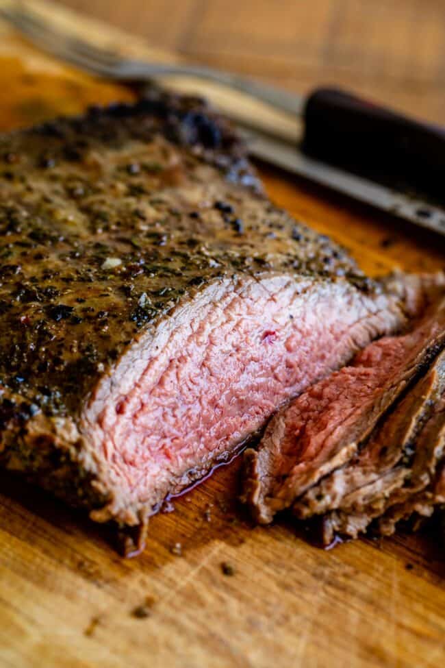 How to Cook Flank Steak (Grilled or Oven Broiled) from The Food Charlatan. Flank Steak is incredibly tasty when done well, but can be really easy to mess up. I will show you all my tips to get a flavorful, juicy, and tender flank steak, grilled outside or under the broiler! Using a great marinade, slicing correctly, and cooking hot and fast are the secrets to a fabulous flank steak. #flank #flanksteak #steak #beef #grill #grilled #easy #recipe #summer #marinade #oven #howtocook #chimichurri sliced grilled flank steak on a wooden cutting board next to grill tools.