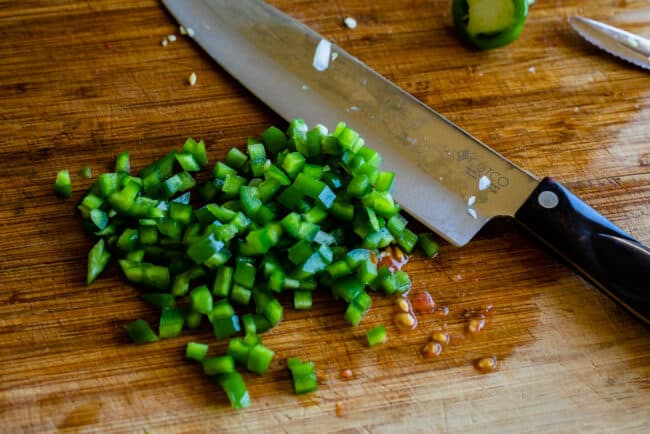 How to Make Authentic Pico de Gallo from The Food Charlatan. Learn how to make the best Pico de Gallo! It's a very simple Mexican salsa with tomatoes, onions, jalapeno, cilantro, and lime juice. Humble ingredients come together to make one of the best appetizers of all time! You will never look at tacos the same after topping them with this magical stuff. #picodegallo #salsa #Mexican #cold #fresh #appetizer #dip #forparties #easy #recipe #receta #authentic #best #homemade #restaurant #picodegalo finely chopped jalapenos for pico de gallo on a wooden cutting board.