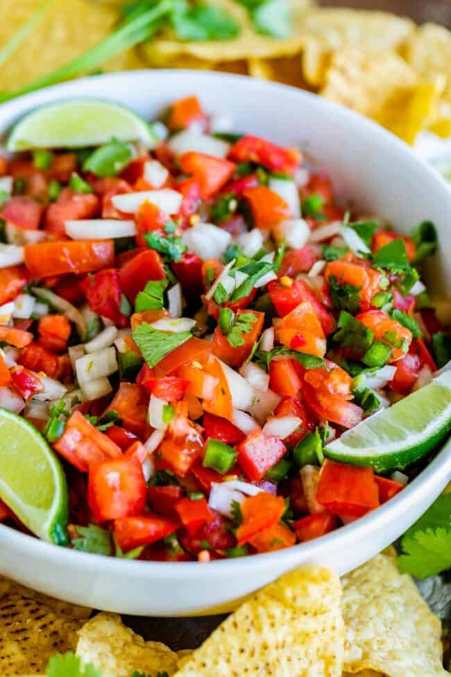 How to Make Authentic Pico de Gallo from The Food Charlatan. Learn how to make the best Pico de Gallo! It's a very simple Mexican salsa with tomatoes, onions, jalapeno, cilantro, and lime juice. Humble ingredients come together to make one of the best appetizers of all time! You will never look at tacos the same after topping them with this magical stuff. #picodegallo #salsa #Mexican #cold #fresh #appetizer #dip #forparties #easy #recipe #receta #authentic #best #homemade #restaurant #picodegalo pico de gallo with lime wedges and tortilla chips.