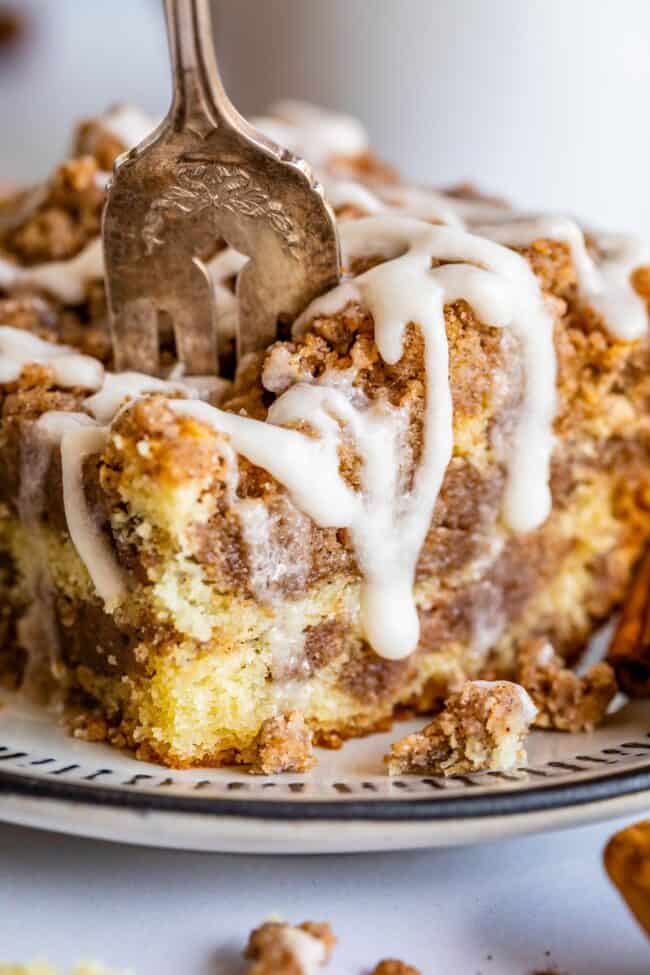 Sour Cream Coffee Cake, with a Ridiculous Amount of Streusel from The Food Charlatan. This is my FAVORITE recipe for Sour Cream Coffee Cake! My main complaint with Coffee Cake is that there is usually too much cake, not enough streusel. This recipe gives you the max amount of streusel without ruining the light fluffiness of the cake! A vanilla drizzle finishes it off! #coffeecake #sourcream #icing #frosting #drizzle #easy #recipes #cinnamon #streusel #sourcream #crumb #crumble #moist #breakfast cinnamon streusel coffee cake on a plate with a fork stuck in it.