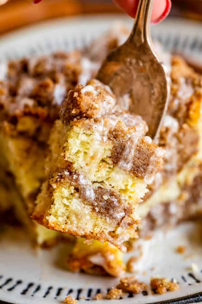 Sour Cream Coffee Cake, with a Ridiculous Amount of Streusel from The Food Charlatan. This is my FAVORITE recipe for Sour Cream Coffee Cake! My main complaint with Coffee Cake is that there is usually too much cake, not enough streusel. This recipe gives you the max amount of streusel without ruining the light fluffiness of the cake! A vanilla drizzle finishes it off! #coffeecake #sourcream #icing #frosting #drizzle #easy #recipes #cinnamon #streusel #sourcream #crumb #crumble #moist #breakfast Slice of coffee cake with streusel and glaze on a fork.