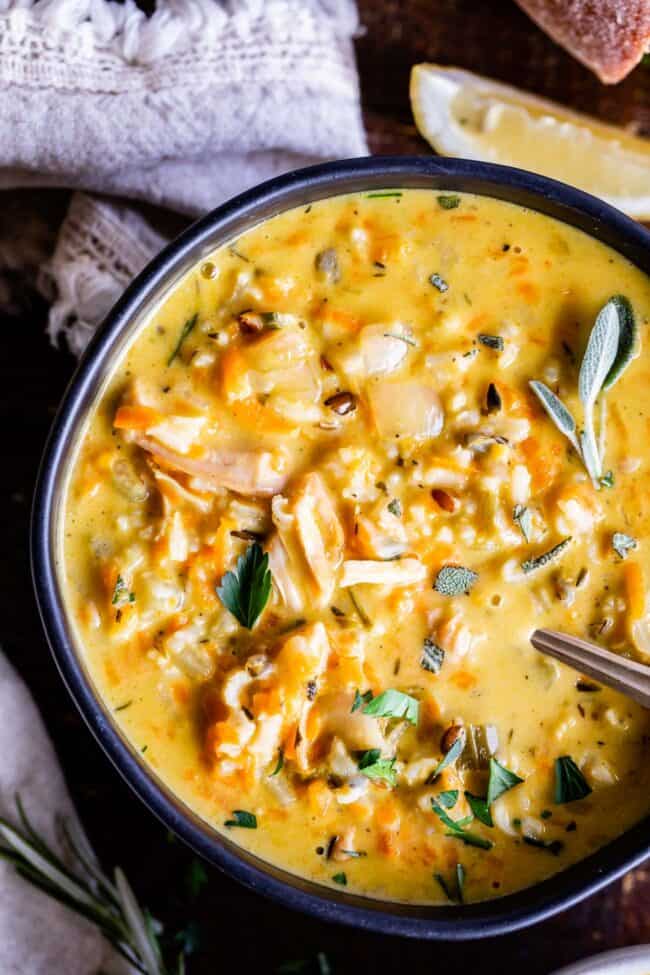 Creamy Turkey Wild Rice Soup recipe from The Food Charlatan! Use your leftover turkey and herbs from Thanksgiving to make a satisfying and healthy soup that is just what you need after all the carb loading you did on Thursday. (I know you.) The hint of lemon and the shredded carrots make this soup really unique and flavorful! #turkey #thanksgiving #christmas #broth #stock #carrots #creamy #crockpot #slowcooker #recipes #leftover #easy #healthy #homemade #carrots #lemon #leftovers #stovetop turkey and rice soup in a bowl with spoon
