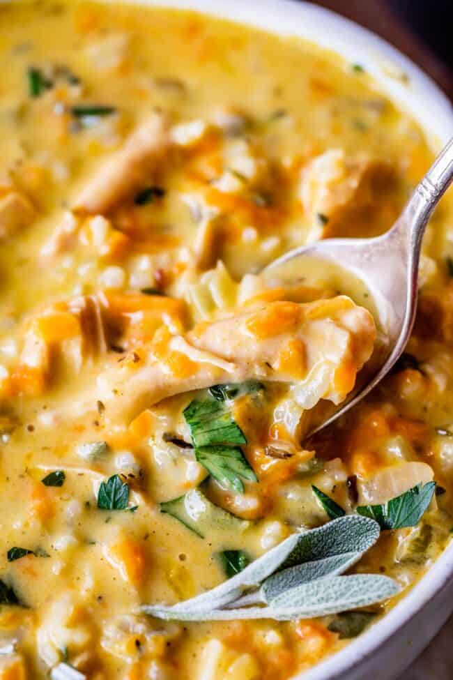 Creamy Turkey Wild Rice Soup recipe from The Food Charlatan! Use your leftover turkey and herbs from Thanksgiving to make a satisfying and healthy soup that is just what you need after all the carb loading you did on Thursday. (I know you.) The hint of lemon and the shredded carrots make this soup really unique and flavorful! #turkey #thanksgiving #christmas #broth #stock #carrots #creamy #crockpot #slowcooker #recipes #leftover #easy #healthy #homemade #carrots #lemon #leftovers #stovetop creamy turkey wild rice soup in a white bowl with a spoon