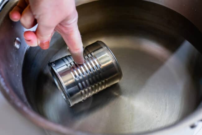adding a can of sweetened condensed milk to a pot of water for making dulce de leche.