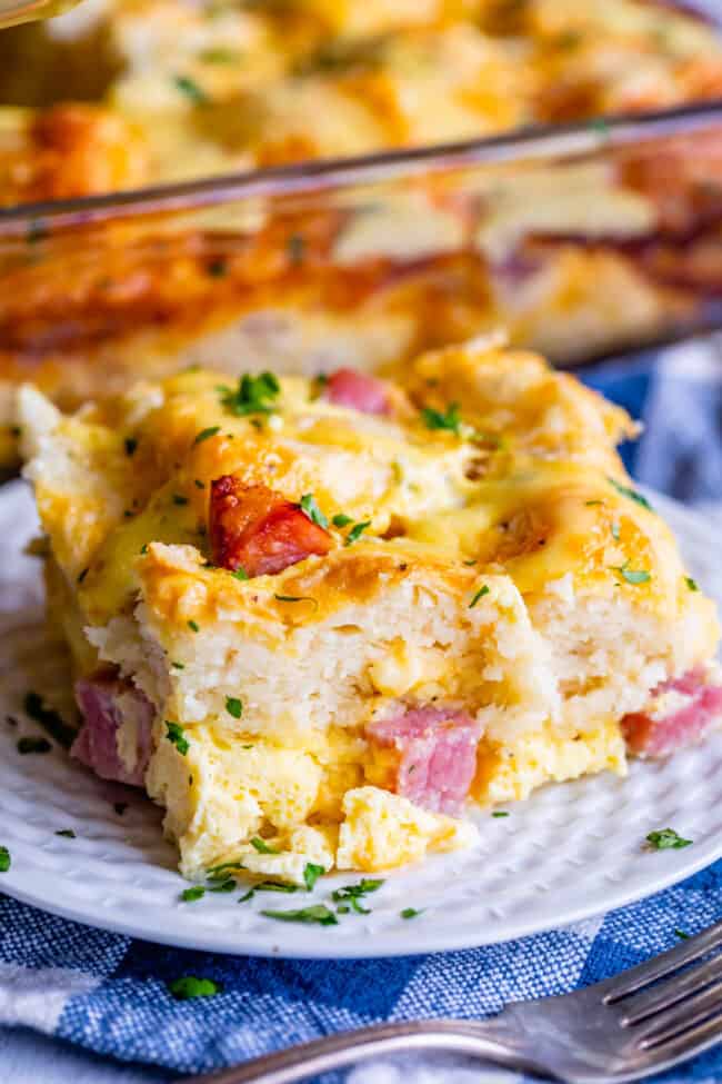 Cheesy Ham and Egg Breakfast Casserole with Biscuits from The Food Charlatan. This crowd-pleasing casserole is my new favorite! Use store bought or homemade biscuits to make a moist and delicious brunch. Top it all off with Hollandaise Sauce for an amazing holiday breakfast! #breakfast #brunch #ham #bacon #sausage #easy #recipe #holidays #Thanksgiving #Christmas #makeahead #withbiscuits #overnight #recipes #foracrowd #best #nightbefore #simple #quick #forlargegroups #Pillsbury #freezer #savory a slice of ham, egg, and cheese biscuit casserole on a plate.